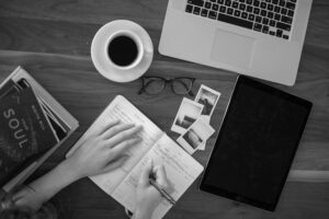 a content writer, writing in a notebook with a cup of coffee, a laptop and a tablet on table